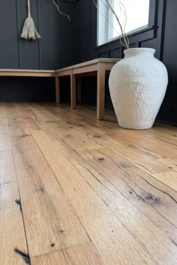 Reclaimed oak wide plank flooring with nail holes and stress cracks in a modern entry way with dark paneled walls.