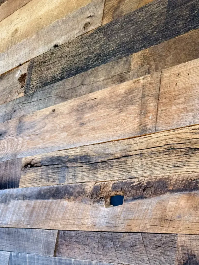 Detailed close-up of weathered reclaimed barn wood planks featuring an original square fastener hole and deep saw marks. This shot illustrates the authentic, high-character grain and varied brown patina of salvaged barnwo