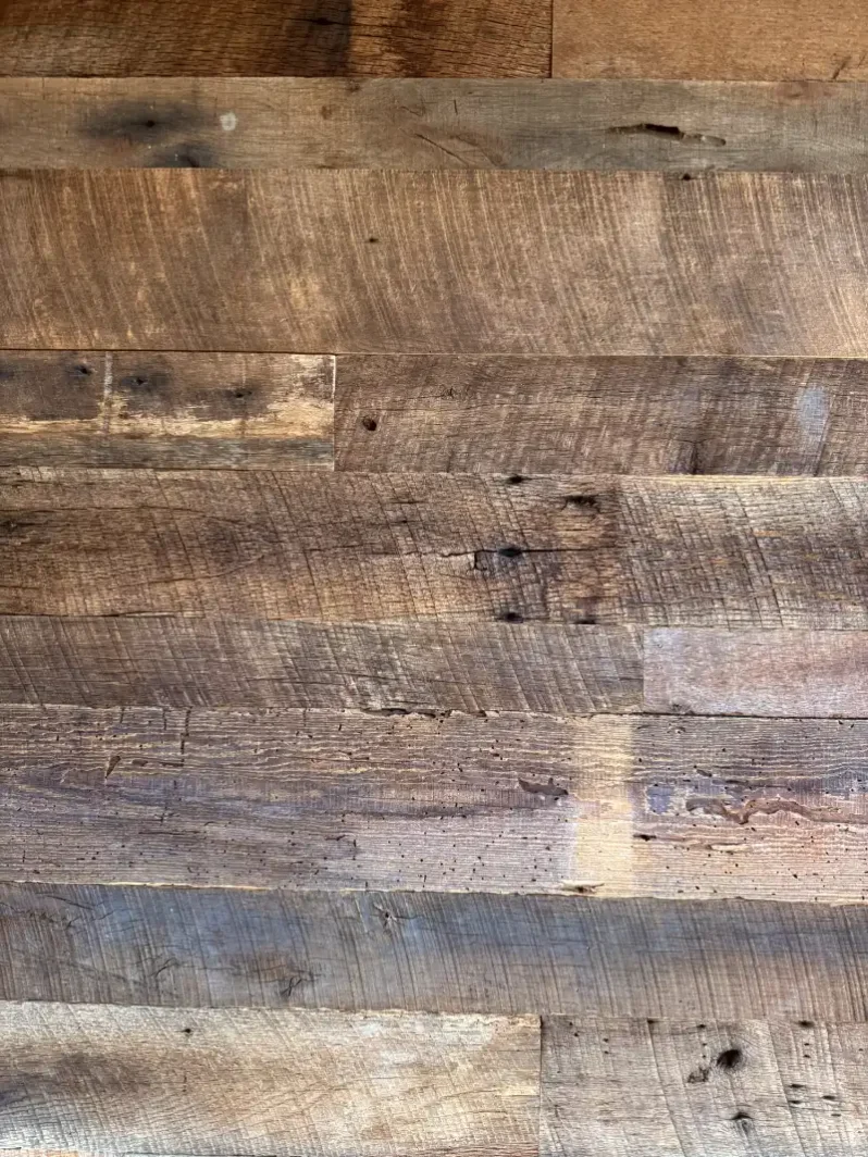 Close-up view of stacked 'Brown Board' reclaimed barn wood planks. This highly detailed shot features original circular saw marks, varied deep brown patinas, and natural weathering highlights, illustrating the authentic rough texture of the wall cladding.