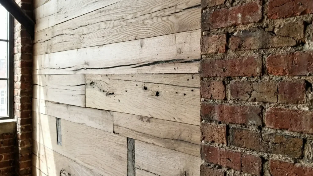 Architectural close-up showing the flush transition between horizontal reclaimed oak cladding and rough exposed brick. The detail emphasizes the precision milling, tight seams, and natural checking of the beam-sawn timber.