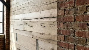 Architectural close-up showing the flush transition between horizontal reclaimed oak cladding and rough exposed brick. The detail emphasizes the precision milling, tight seams, and natural checking of the beam-sawn timber.