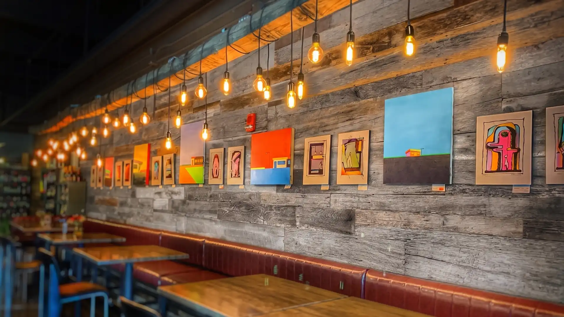 Reclaimed weathered gray wood cladding in a modern cafe/wine bar featuring Edison bulb lighting and colorful art.