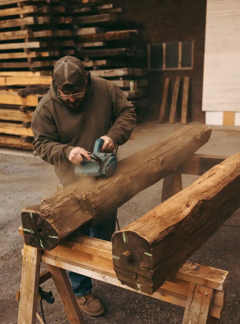 Wes sanding a thick reclaimed barn beam at our woodshop to create a custom fireplace mantel.