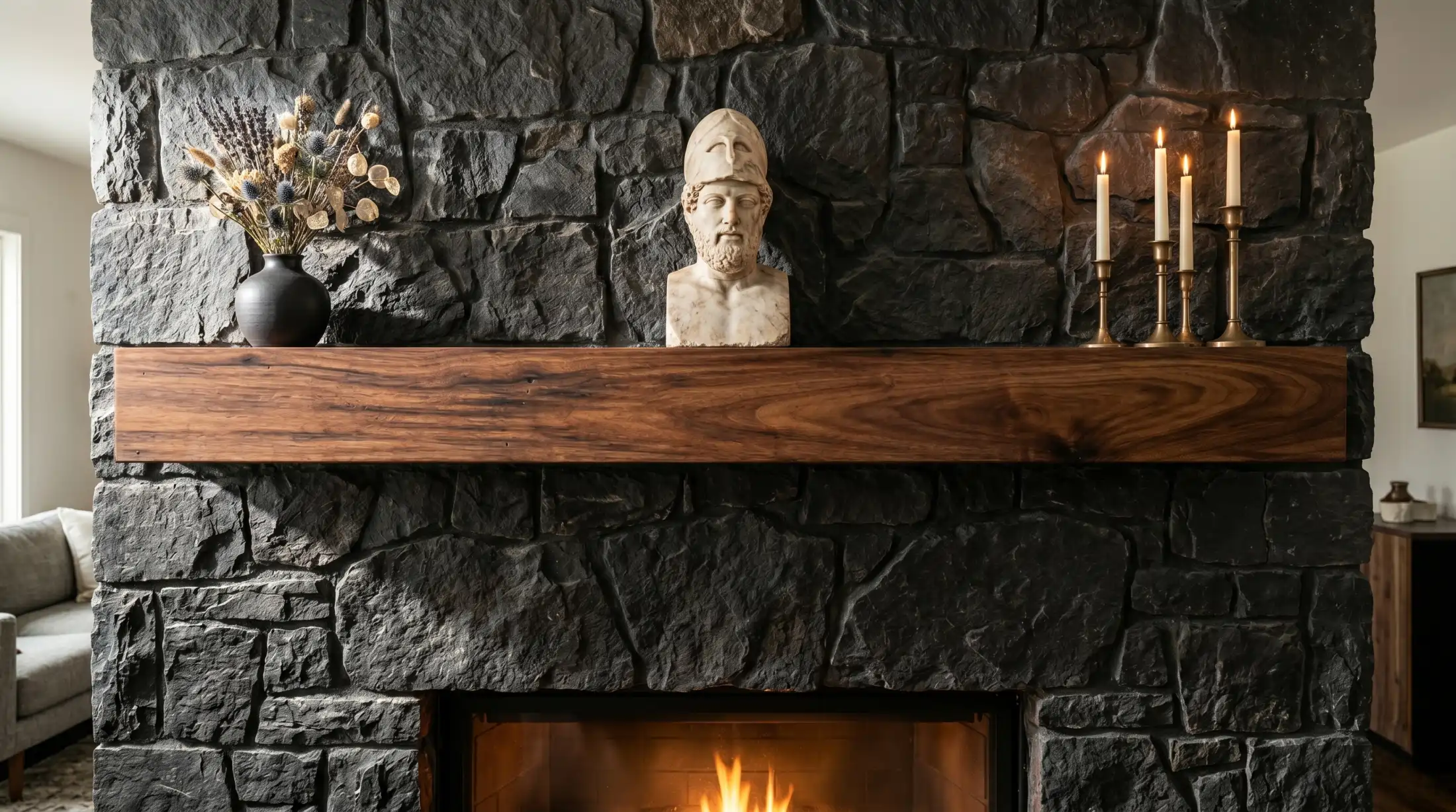 Custom Walnut floating shelf mantel on a dark stone fireplace with Greek bust art on top, candles and a black vase with flowers.