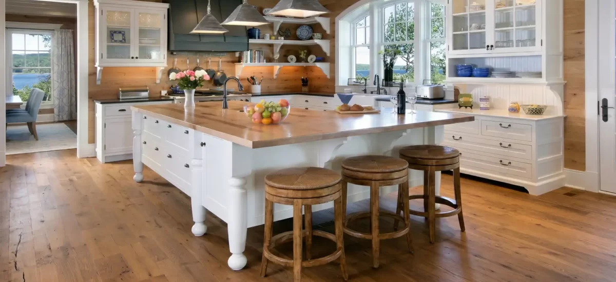 Reclaimed oak wide plank flooring with nail holes and stress cracks in a bright custom kitchen with white cabinets.