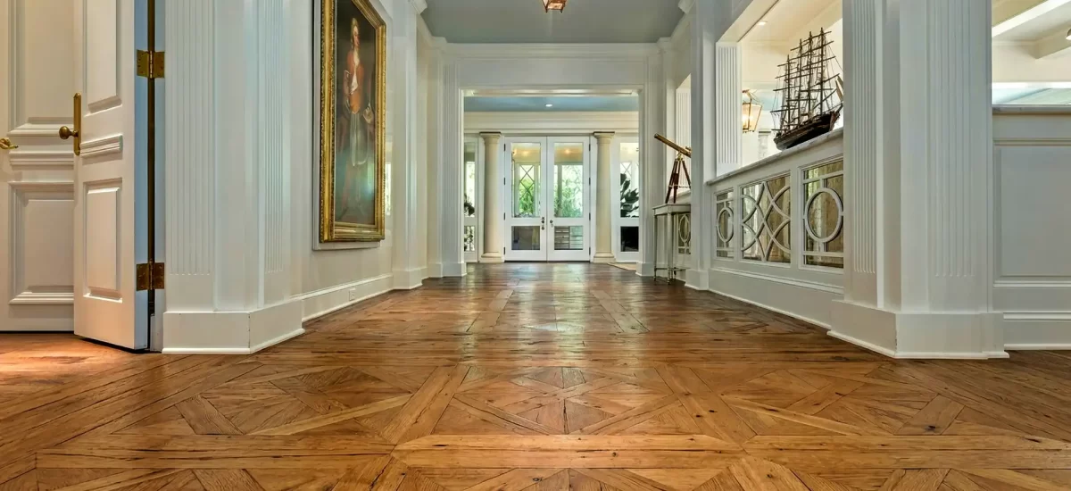 Reclaimed oak wide plank flooring in a custom parquet pattern with nail holes and stress cracks in a grand white foyer.