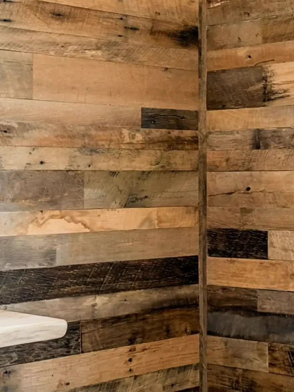 An interior room corner featuring authentic Brown Board reclaimed barnwood planks installed as a wrap-around feature wall. Natural light from a nearby window highlights the varied earthen patina and rustic texture of the historic barn wood wall boards.