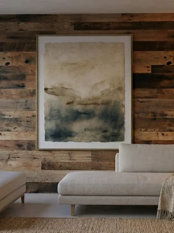Modern living room interior showcasing a large architectural accent wall made of Brown Board reclaimed barnwood planks. The rustic texture of the weathered brown barn wood creates a striking focal point behind a neutral sectional sofa and framed artwork.