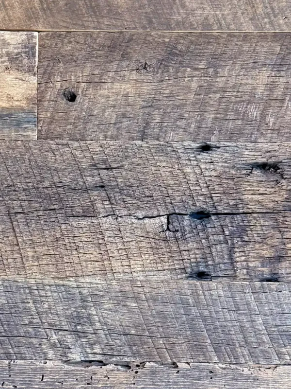Highly detailed close-up of reclaimed barnwood planks showcasing original circular saw marks and a deep, weathered brown patina. Small fastener holes and natural wood grain illustrate the authentic history of these antique barn wood wall boards.