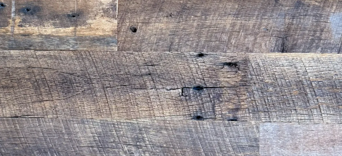 Highly detailed close-up of reclaimed barnwood planks showcasing original circular saw marks and a deep, weathered brown patina. Small fastener holes and natural wood grain illustrate the authentic history of these antique barn wood wall boards.