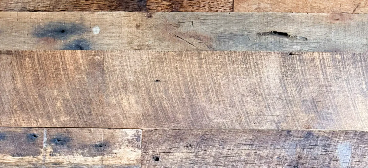 A group of several Brown Board reclaimed barnwood planks displayed side-by-side. The image illustrates the beautiful range of deep chocolate to warm tan patinas, varied width options, and authentic original face textures found in this unique collection.