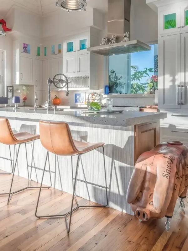 Antique wormy chestnut flooring in a bright coastal kitchen featuring white cabinetry and leather barstools.