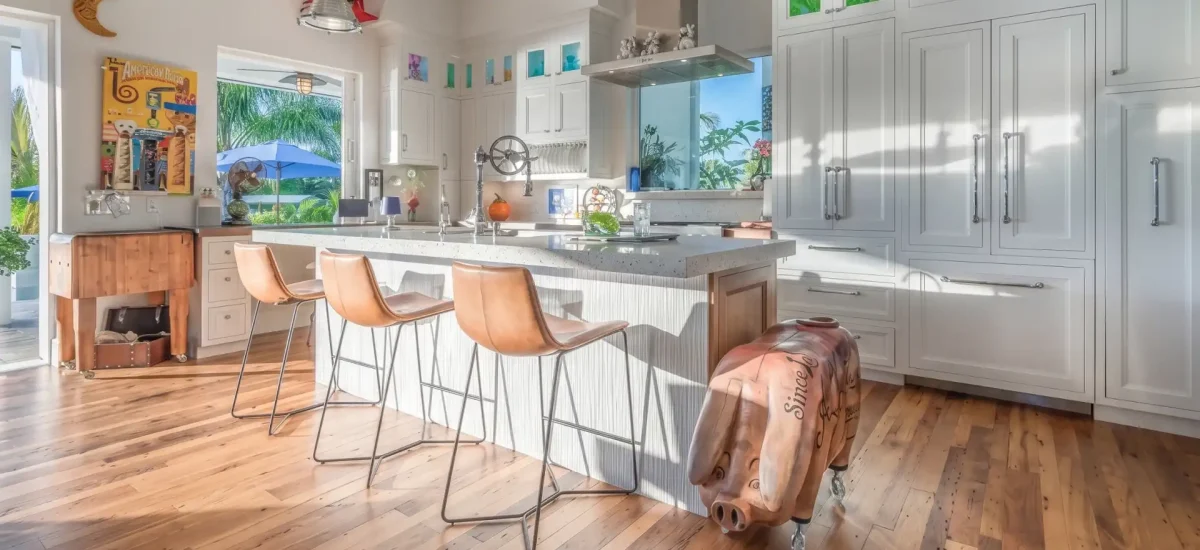 Antique wormy chestnut flooring in a bright coastal kitchen featuring white cabinetry and leather barstools.