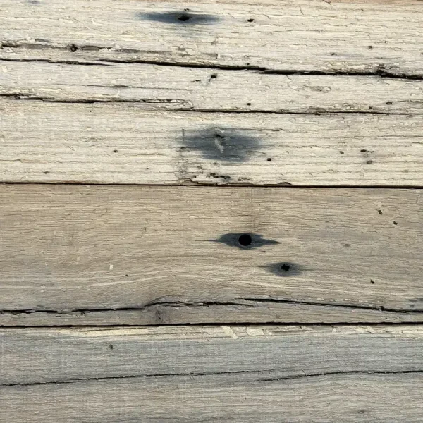 Close-up of dark tannin staining and original nail holes on a light-brown reclaimed oak plank, illustrating its structural history.