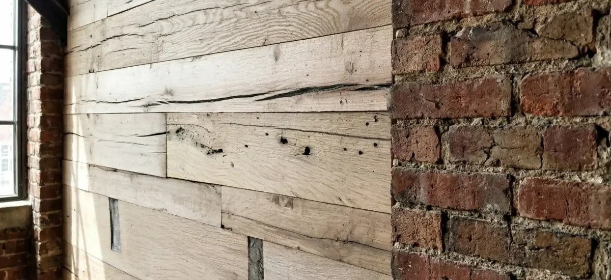 Architectural close-up showing the flush transition between horizontal reclaimed oak cladding and rough exposed brick. The detail emphasizes the precision milling, tight seams, and natural checking of the beam-sawn timber.